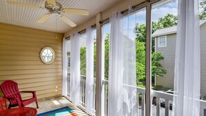 Une véranda couverte avec un ventilateur de plafond, une chaise Adirondack rouge, une table ronde et un tapis coloré.