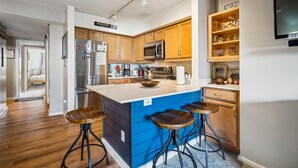 Una cocina moderna con armarios de madera, un refrigerador de acero inoxidable, un microondas y una isla grande con taburetes.