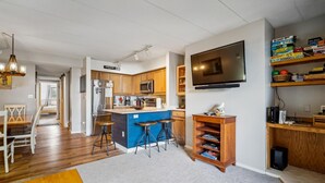 Una cocina moderna con una isla central, taburetes de bar, un televisor de pantalla plana y una estantería.