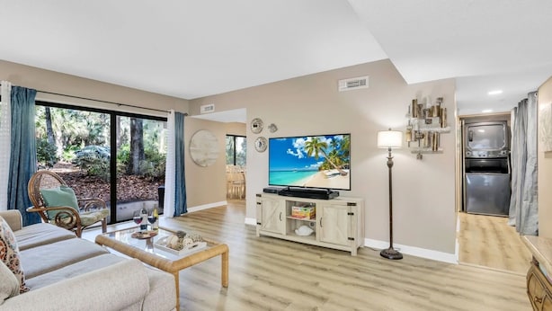 A living room with a TV, wooden flooring, a dining area, and a kitchen with a fridge and oven. - Coastal Comfort Escape Close to Beach & Eats (Hilton Head Island)