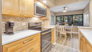 A modern kitchen with wooden cabinets, a built-in microwave, a Keurig coffee maker, and a dining area with a table and chairs. - Coastal Comfort Escape Close to Beach & Eats (Hilton Head Island)