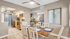 A modern kitchen with a microwave, oven, and refrigerator. There is a dining area with a table set for four, chairs, and a vase with flowers. - Coastal Comfort Escape Close to Beach & Eats (Hilton Head Island)