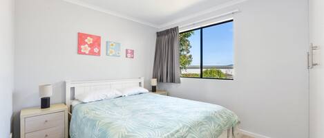 A bedroom with a bed, nightstands, a window with a view, and wall art.