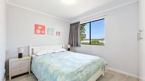 A bedroom with a bed, nightstands, a window with a view, and wall art.