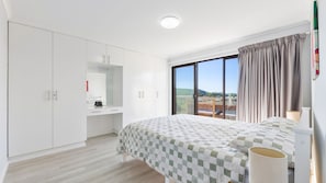 A bedroom with a large bed, a wardrobe, a desk, and a window with a view.