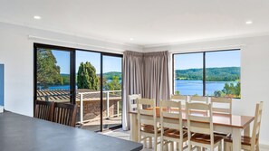 A dining area with a table and chairs, large windows with a view of a lake and trees, and a balcony with a railing.