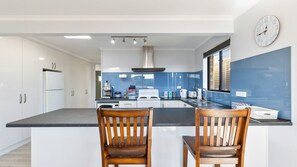 A modern kitchen with white cabinets, a blue backsplash, a central island, and two wooden chairs.