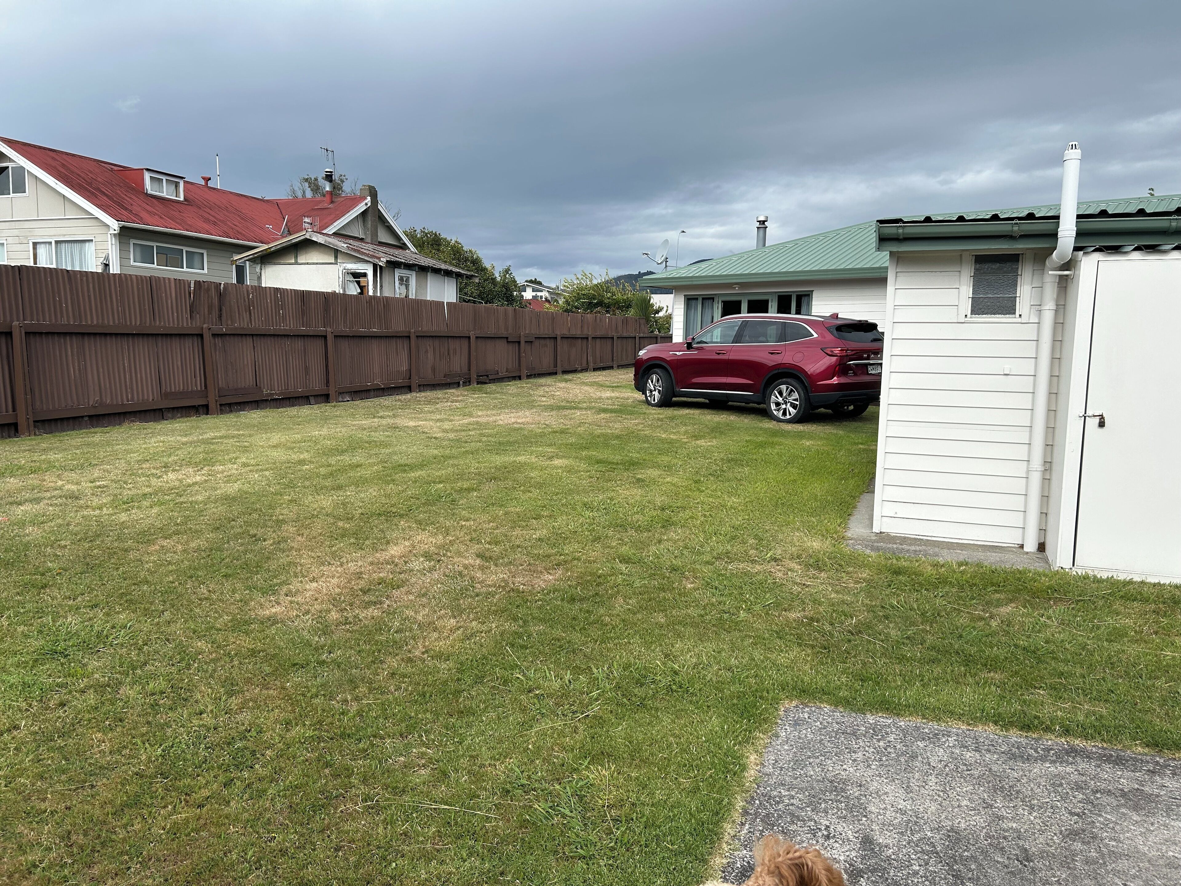 A backyard with a red SUV parked, a wooden fence, and a shed.