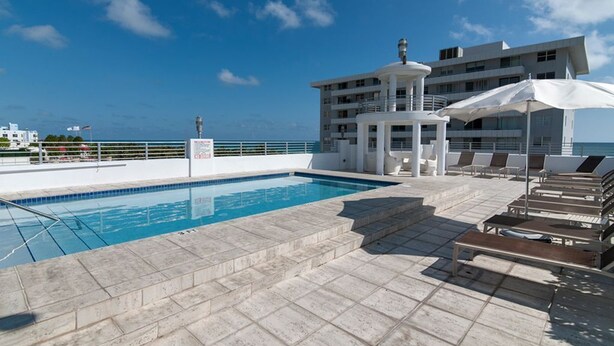 A rooftop pool area with a clear view of the ocean, a lounge with sunbeds, and a multi-story building in the background. - Miami Beach Luxury on South Beach Suite 303 (Miami Beach)