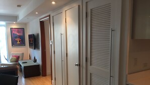 A modern room with a wooden floor, a desk, a chair, and a television. There are two doors and a window with blinds. - Miami Beach Luxury on South Beach Suite 303 (Miami Beach)