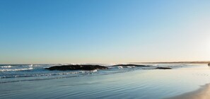 A beach with calm waves, a clear sky, and a logo for 'The Bay Holiday Properties'. - Pacific Paradise No.28 Anna Bay - New Home Close to Birubi Beach (ANNA BAY)