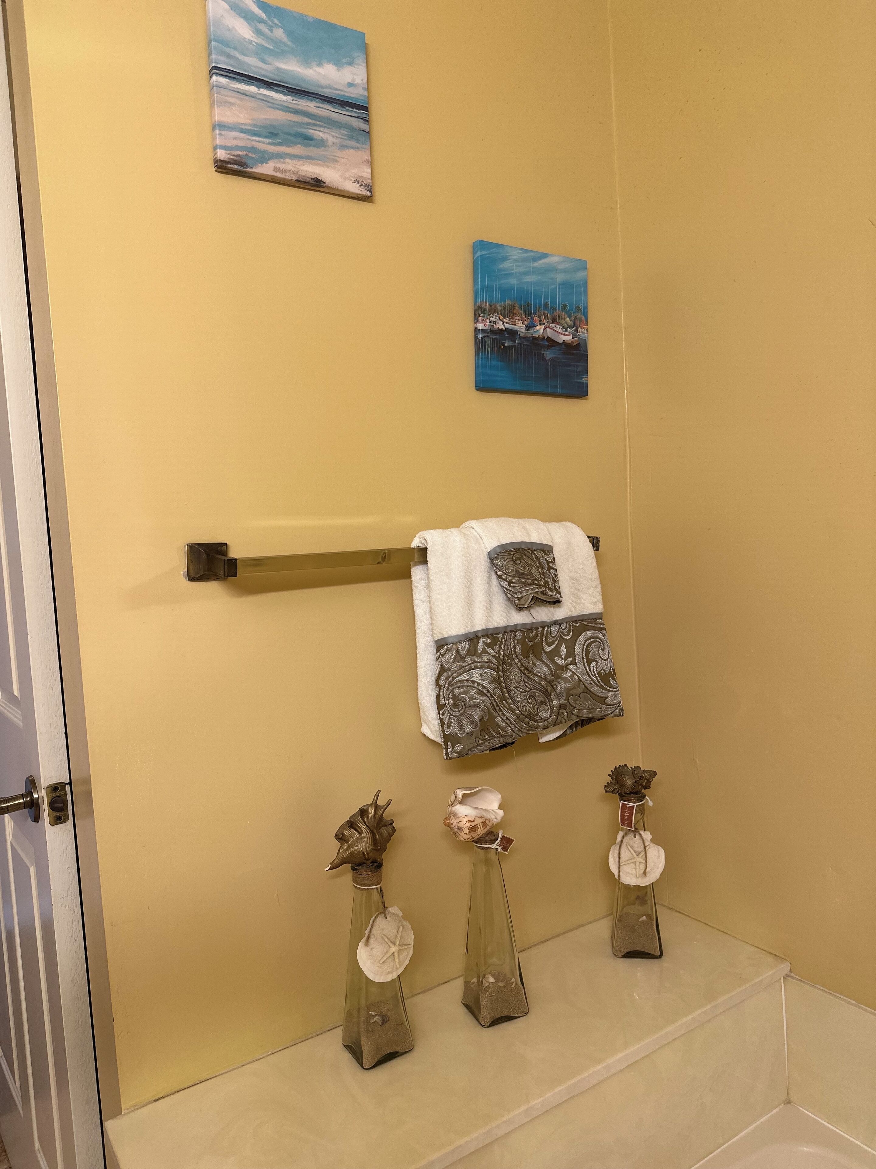 A bathroom with a yellow wall, a towel rack with two towels, and two decorative vases with seashells.