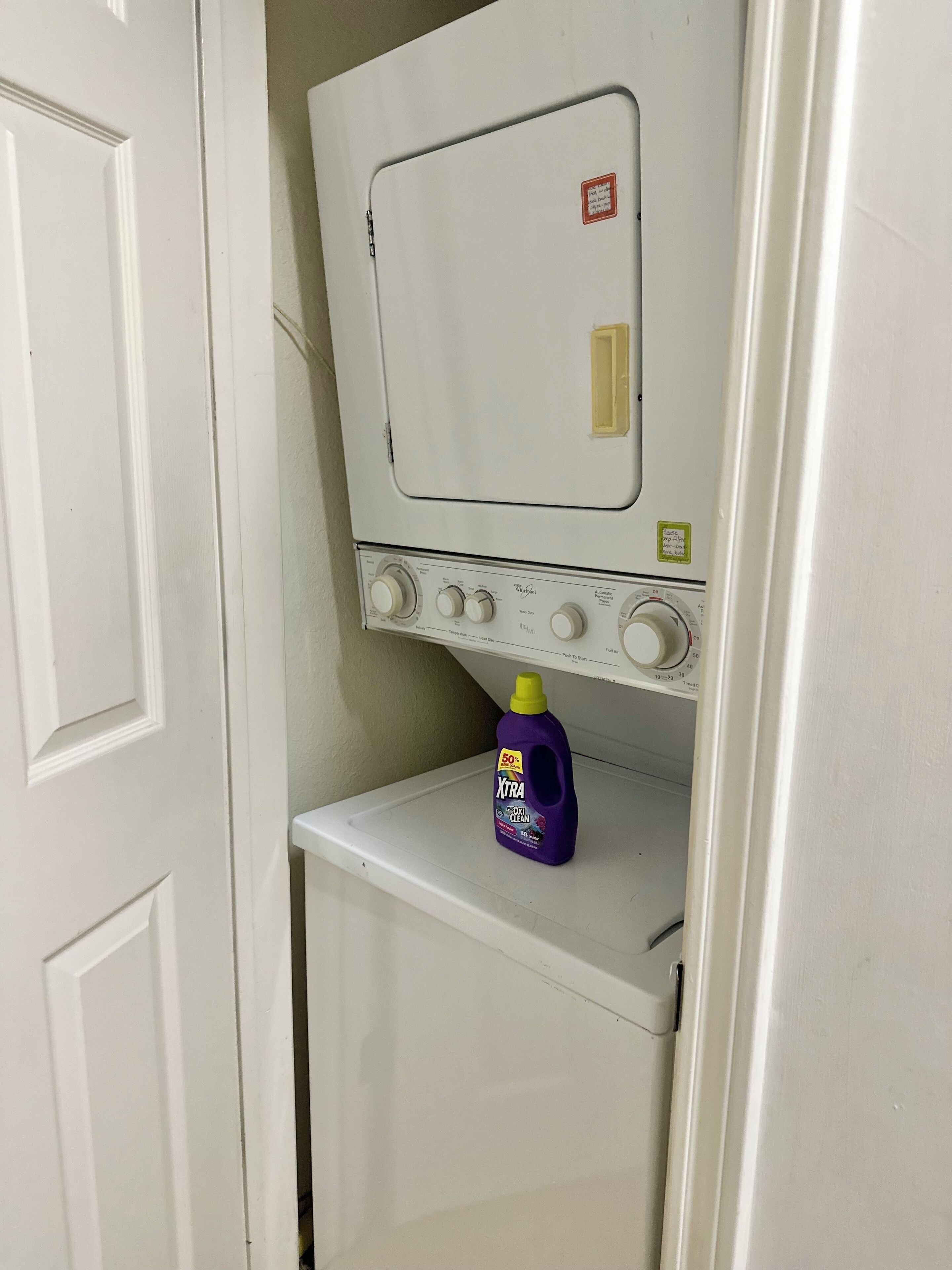 A compact washer and dryer unit with a single detergent bottle on the lower shelf.