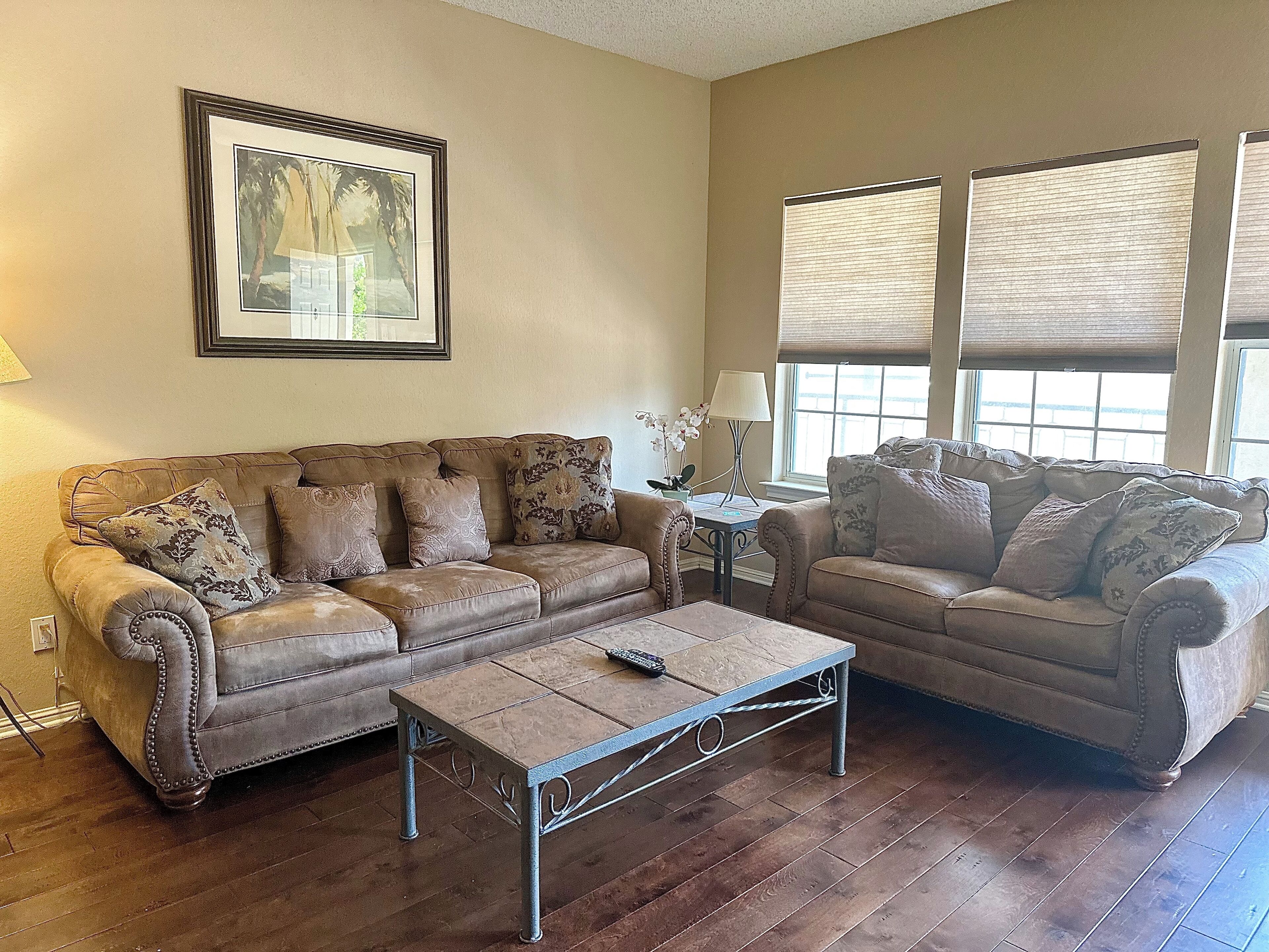 A living room with two leather sofas, a coffee table, a framed picture on the wall, and a window with blinds.