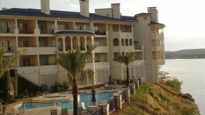 A multi-story hotel with balconies, a swimming pool, and a view of the water. - Luxury Condo on its Own Private Island on Lake Travis (Lago Vista)