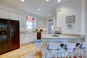 A modern kitchen with white cabinets, a black refrigerator, a granite countertop, and a seating area with white chairs. - Pet friendly short walk to the beach! (Rehoboth Beach)