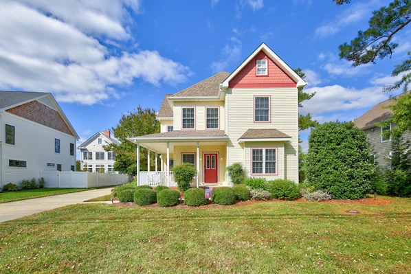 A two-story house with a red front door, a covered porch, and a well-maintained lawn. - Pet friendly short walk to the beach! (Rehoboth Beach)