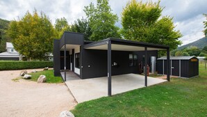 Un bâtiment moderne en métal noir, doté d’un espace extérieur couvert, d’une allée en gravier et d’une pelouse bien entretenue.