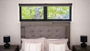 Une chambre à coucher avec un lit, deux lampes de chevet, une fenêtre donnant sur la forêt et une tête de lit texturée.