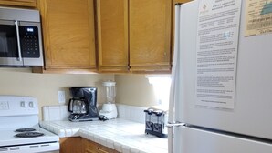 Une cuisine avec des meubles de rangement en bois, un réfrigérateur blanc, une cuisinière, une machine à café et un four à micro-ondes.