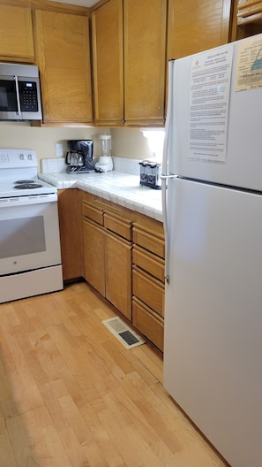 A kitchen with wooden cabinets, a white refrigerator, a stove, a coffee maker, and a microwave. - Snowcreek Resort Vacation Rental 871 (Mammoth Lakes)
