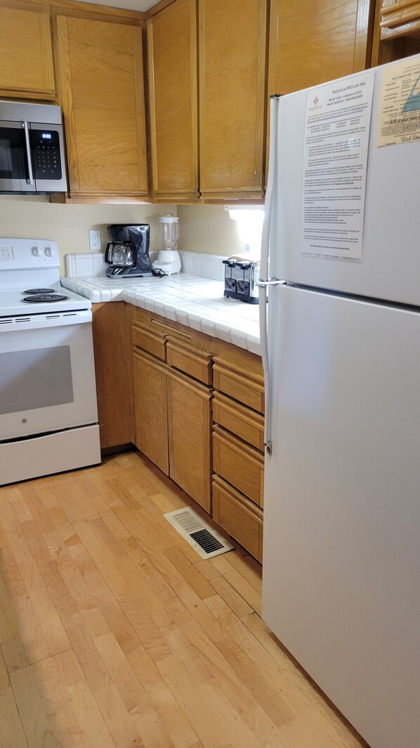 Una cocina con armarios de madera, un refrigerador blanco, estufa, cafetera y microondas.