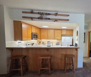 A kitchen with wooden cabinets, a microwave, a refrigerator, and a bar area with stools. - Snowcreek Resort Vacation Rental 871 (Mammoth Lakes)