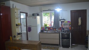 Eine kleine Küche mit Kühlschrank, Herd und Spüle. Im Vordergrund steht ein Holztisch und ein Stuhl.