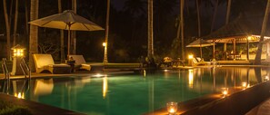 A nighttime pool area with lounge chairs and umbrellas, surrounded by palm trees. - Three oceanfront luxury villas with sauna and tennis court (Sengkidu)
