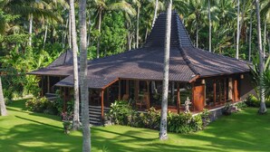 A traditional-style building with a steeply pitched roof, surrounded by lush greenery and palm trees.