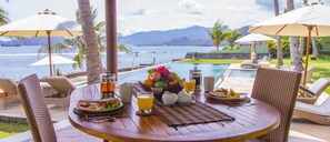 A wooden table with breakfast items, a view of the ocean, and lounge chairs with umbrellas. - Three luxury villas, beachfront/sauna, tennis court + free airport shuttle (Sengkidu)