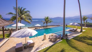 A pool area with lounge chairs, umbrellas, and a view of the ocean.