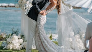 A couple embracing at a seaside wedding ceremony with floral decorations and a clear view of the ocean.