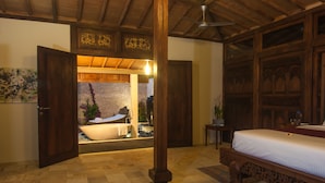 A room with a wooden ceiling, a bed with a white bedspread, a stone wall, and a bathtub.