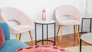 A modern living room with two pink chairs, a small round table with a bottle and glasses, and a glass coffee table.