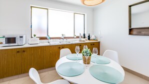 A modern kitchen with a white countertop, wooden cabinets, a large window, and a dining area with a white table and chairs.