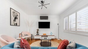 A modern living room with a blue sofa, a small round table, a flat-screen TV, and a ceiling light fixture.