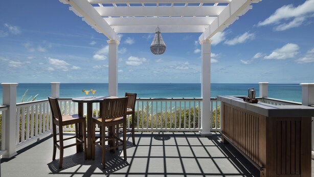 A covered outdoor area with a table and chairs, a hanging light fixture, and a view of the ocean. - Compound w/Beach, Pool,  PICKLEBALL, Gym, Kayaks, Golf Carts, VIEWS! (Governor's Harbour)