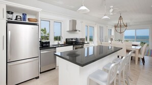 A modern kitchen with a large island, stainless steel appliances, and a view of the ocean. - Compound w/Beach, Pool,  PICKLEBALL, Gym, Kayaks, Golf Carts, VIEWS! (Governor's Harbour)