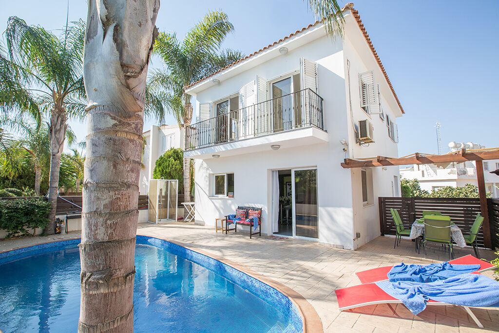 A two-story house with a balcony, a swimming pool, and outdoor furniture.