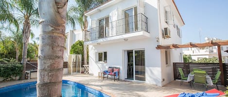 A two-story house with a balcony, a swimming pool, and outdoor furniture.