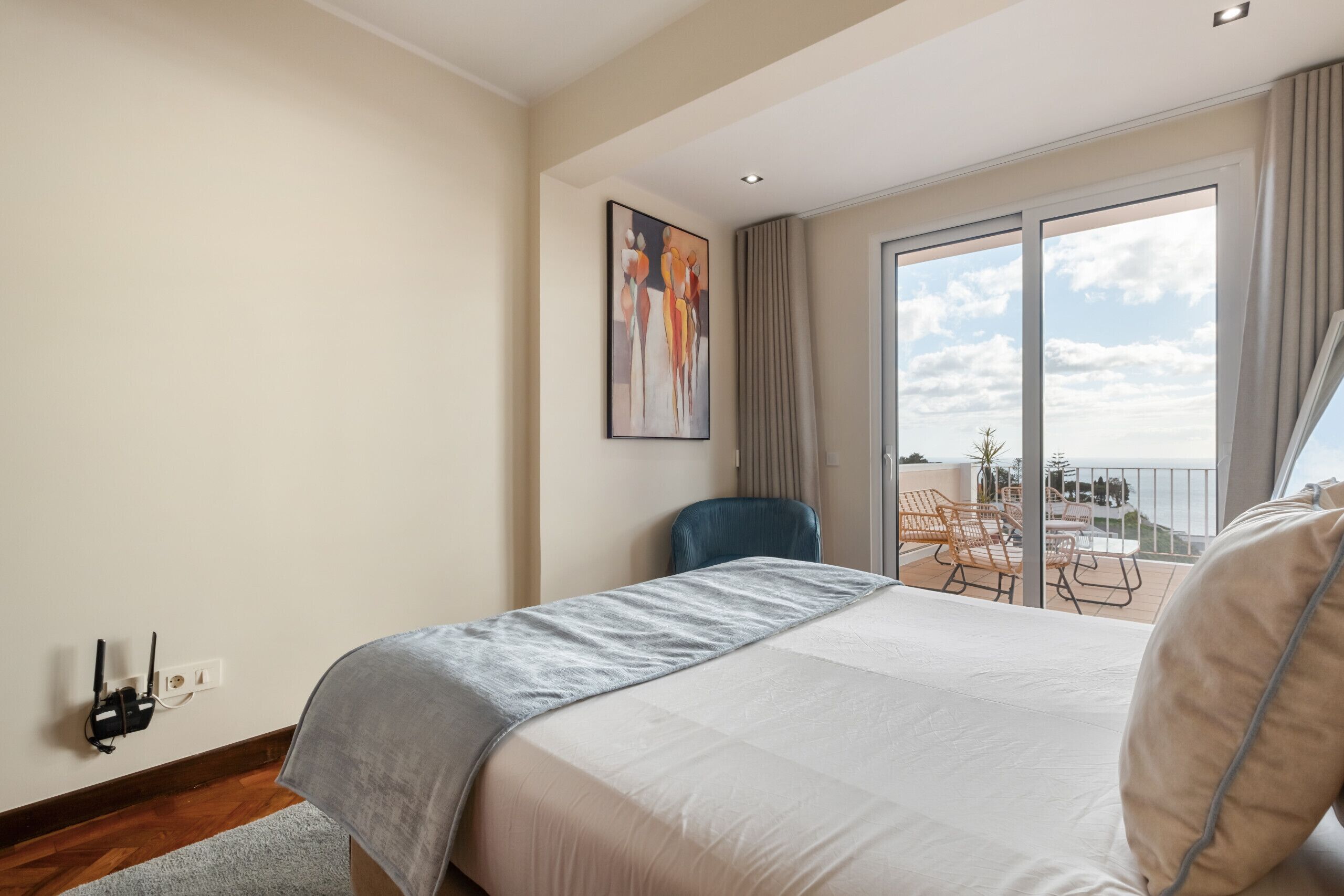 Habitación de hotel con cama, una silla, un cuadro y balcón con mobiliario exterior.