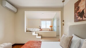A bedroom with a bed, a white chair, a red rug, a staircase leading to a balcony, and an air conditioning unit. - Funchal Bay View Villa by Madeira Sun Travel (Funchal)