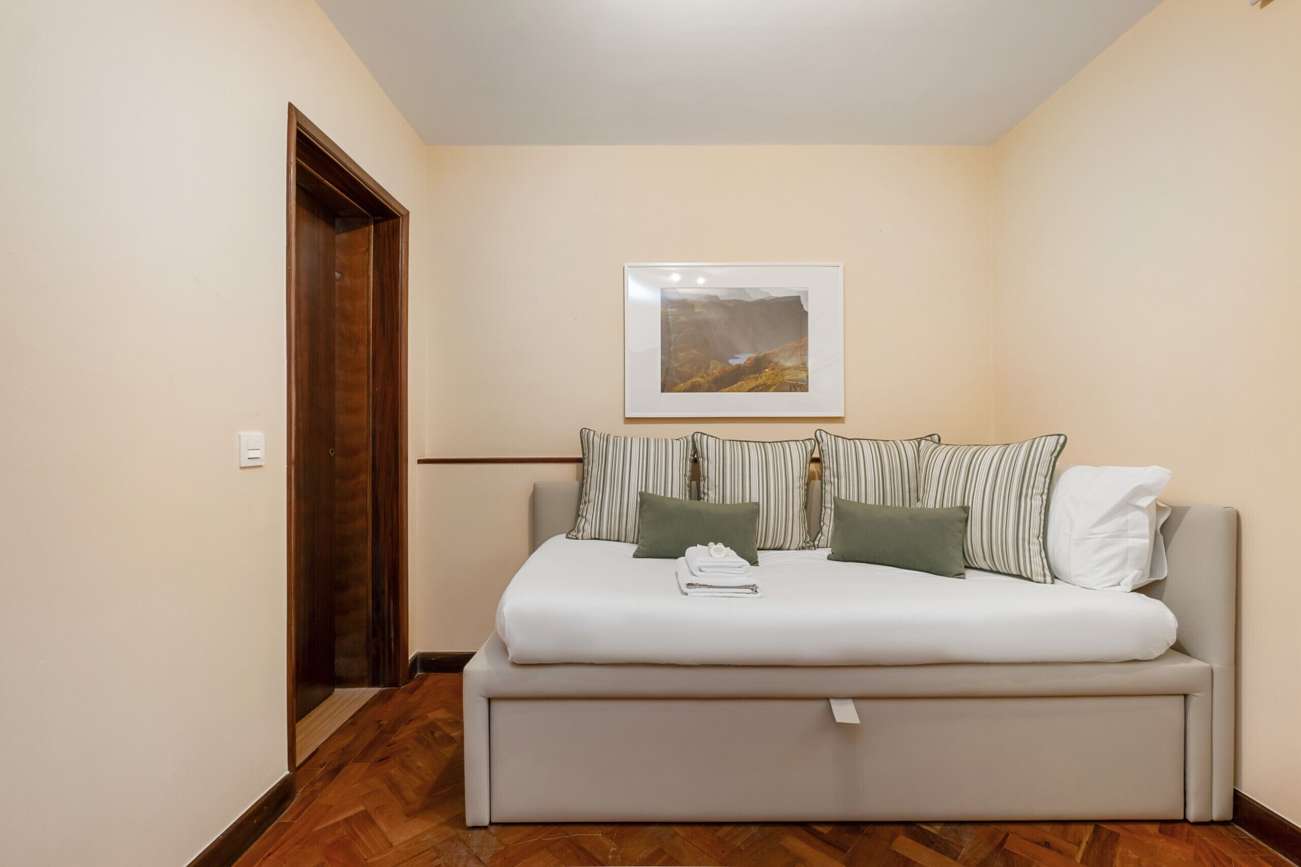A bedroom with a bed, a door, a framed picture on the wall, and a wooden floor.