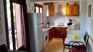 A compact kitchen with a washing machine, a sink, wooden cabinets, and a dining area with a table and chairs.