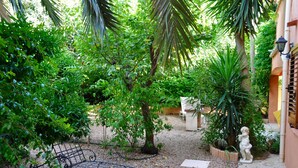 A garden with a metal bench, a statue, and a pathway.