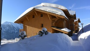 Un chalet en bois, dont le toit est recouvert de neige, se dressant sur un fond de montagnes.