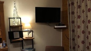 Une petite pièce agréable et chaleureuse, avec un téléviseur fixé au mur, un fauteuil, une petite table et un luminaire décoratif.
