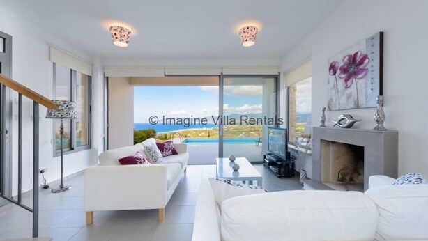 Una sala moderna con un sofá blanco, una chimenea y un ventanal grande con vistas a una piscina.