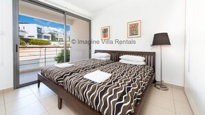 Un dormitorio con una cama grande, un ventanal corredero al balcón y una lámpara de pie.